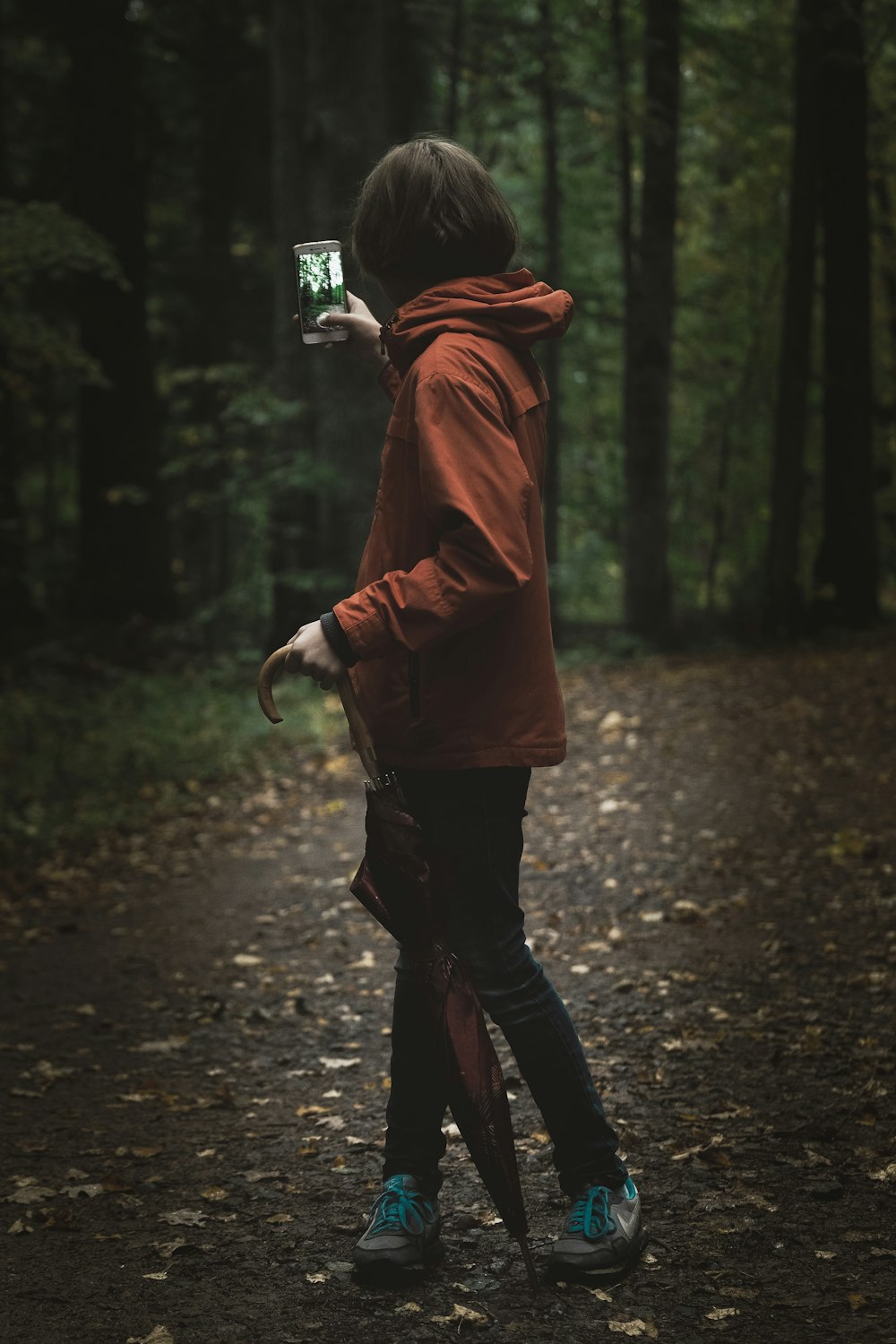donna che indossa una felpa con cappuccio rossa che tiene lo smartphone vicino all'albero a foglia verde