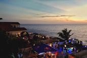 A lively event by the sea with guests enjoying a sunset celebration on a beach terrace.