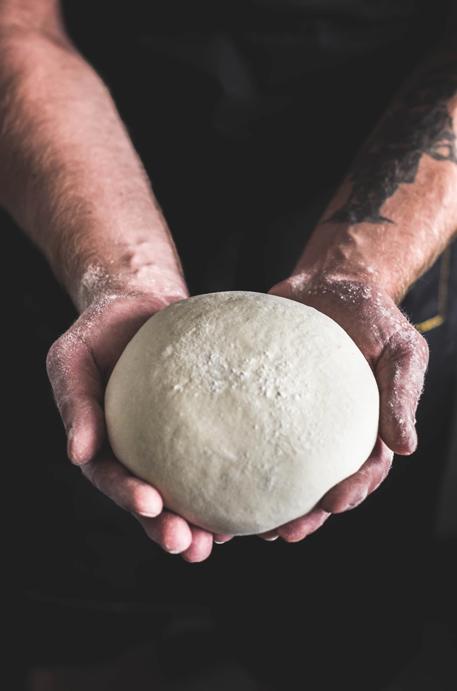A baker's floured hands cradling a round of dough