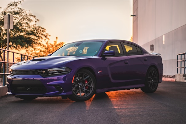 A royal purple sports car with a flawless shine parked on a driveway at dusk, reflecting the metallic gold accents.