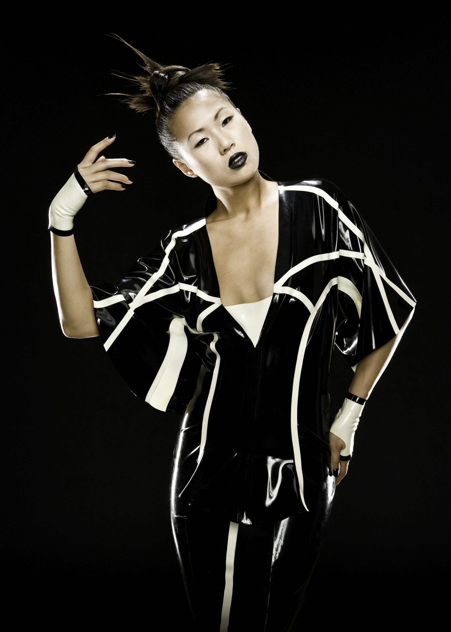 An edgy high-fashion shot featuring a model against a stark black background, styled in avant-garde attire with bold makeup and intense gaze.