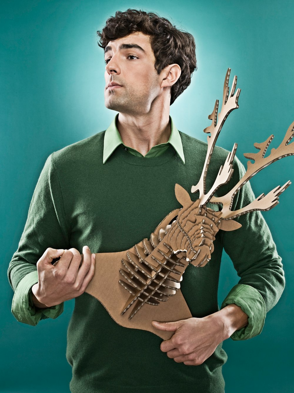 man wearing green sweater holding brown deer head decor