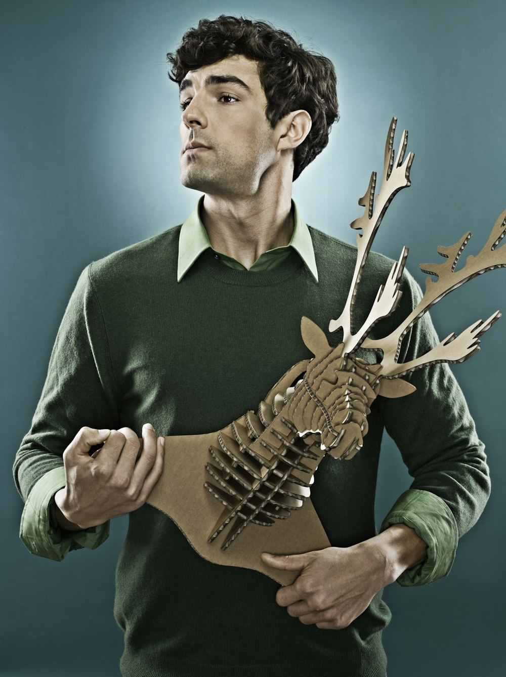 man wearing green sweater holding brown deer head decor