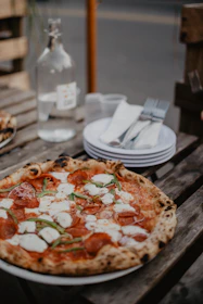 A delicious large pepperoni pizza next to a chilled 1.5L bottle of guaraná soda on a rustic wooden table.
