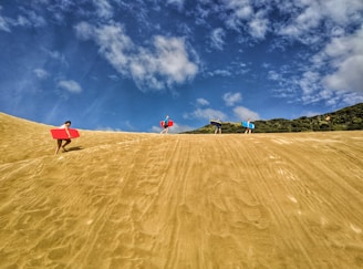 A group of friends carrying colorful inflatable surfboards, laughing on a sunny beach day.