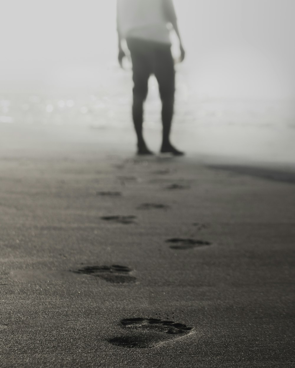 Photographie en niveaux de gris d’un homme marchant sur le sable laissant des empreintes de pas