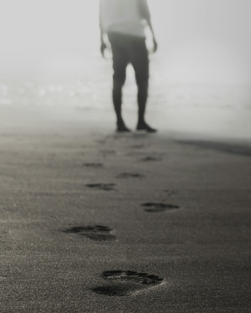 Graustufenfotografie eines Mannes, der auf Sand geht und Fußabdrücke hinterlässt