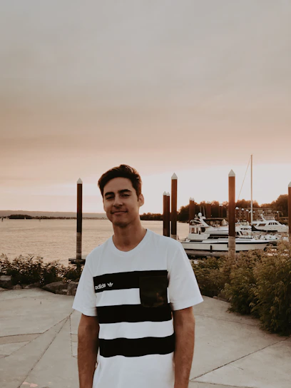 Portrait of Yassin Papito standing by the Mombasa coastline, with ships and the busy port in the background at sunset.