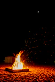Nighttime beach bonfire glowing softly against starry sky.