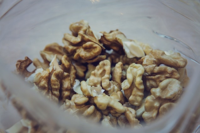 A close-up view of several walnuts inside a transparent glass container. The walnuts are shelled, revealing their intricate patterns and textures. The focus is on the nuts, with a blurred background giving a soft appearance.