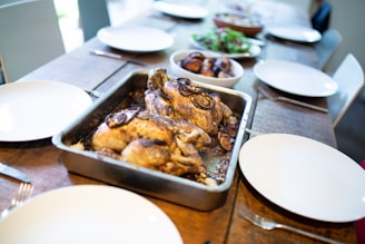 A rustic wooden table with a steaming roasted chicken surrounded by fresh herbs and traditional Mexican side dishes.