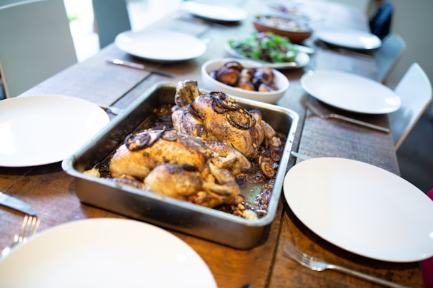 A rustic wooden table with a steaming roasted chicken surrounded by fresh herbs and traditional Mexican side dishes.