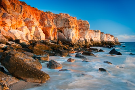 waves crushing on rock boulders along shore beside rocky mountain during daytime in Cape Leveque Australia