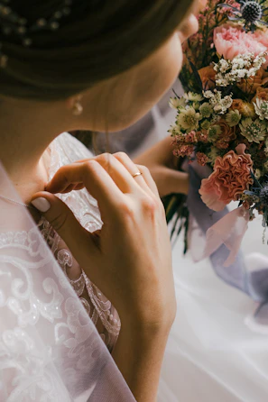 Close-up of intricate wedding details: lace dress sleeve, vintage rings, and fresh blooms.