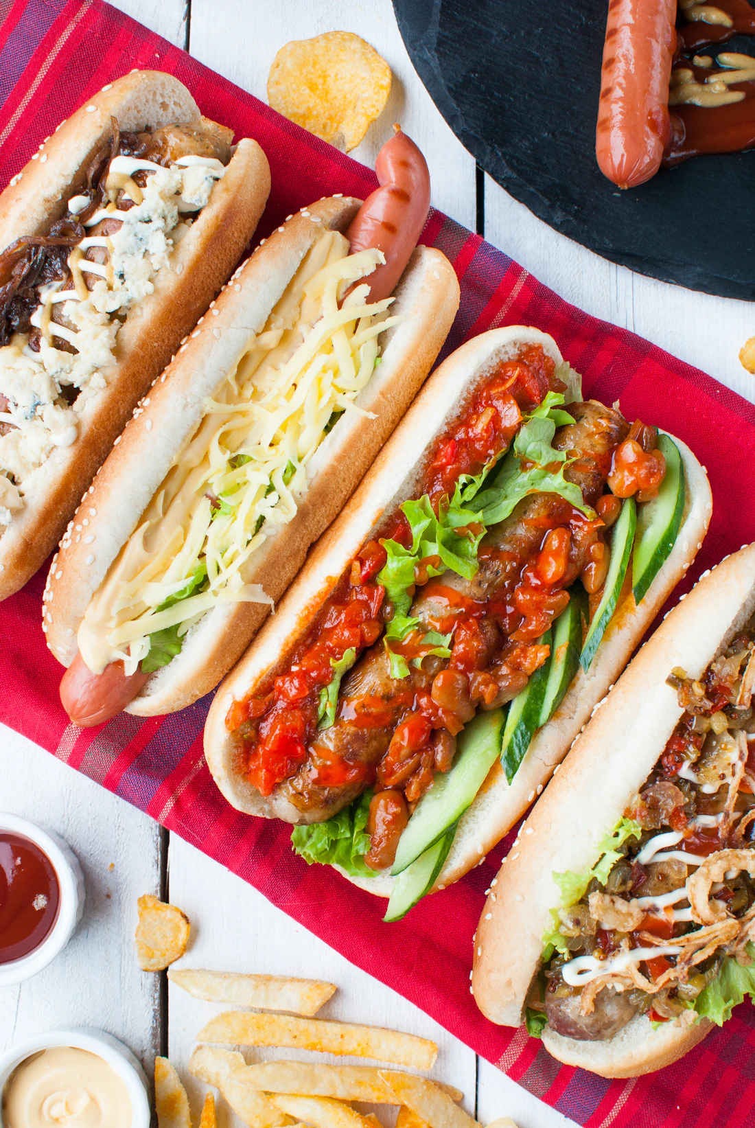 Cuatro hot dogs con distintos ingredientes sobre una mesa