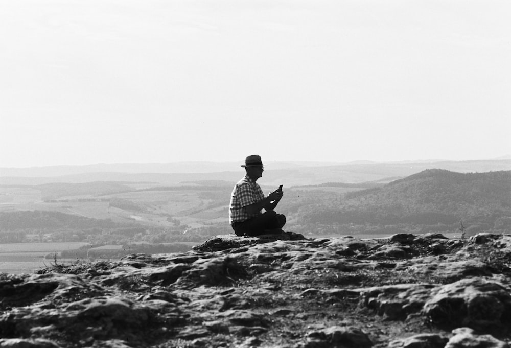 um homem sentado no topo de uma encosta rochosa