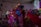 A vibrant scene depicting a traditional dance performance with colorful, floral-patterned costumes. The performers are energetically moving, creating dynamic and flowing patterns with their outfits in a warmly lit indoor setting.