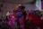 A vibrant scene depicting a traditional dance performance with colorful, floral-patterned costumes. The performers are energetically moving, creating dynamic and flowing patterns with their outfits in a warmly lit indoor setting.