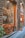 A rustic storefront featuring hanging cured meats inside the window, a large wooden wagon wheel leaning against the glass, and a small chalkboard sign near some potted plants. The exterior is crafted with stonework, and there's an inviting entrance to a restaurant.