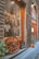 A rustic storefront featuring hanging cured meats inside the window, a large wooden wagon wheel leaning against the glass, and a small chalkboard sign near some potted plants. The exterior is crafted with stonework, and there's an inviting entrance to a restaurant.