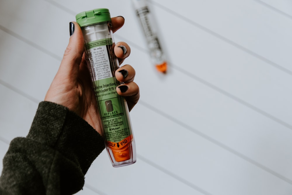 personne tenant une bouteille en verre vert, orange et transparent