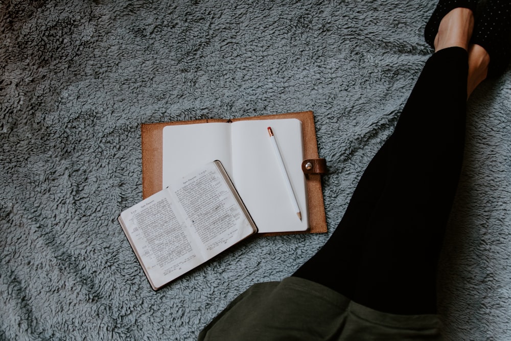 libro bianco aperto posizionato vicino alla gamba della donna su superficie grigia