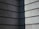 A corner of a building with a modern, minimalist design features horizontal concrete slabs. The surface has a textured appearance, showing light and shadow creating a stark contrast with a diagonal division between light and dark.