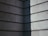 A corner of a building with a modern, minimalist design features horizontal concrete slabs. The surface has a textured appearance, showing light and shadow creating a stark contrast with a diagonal division between light and dark.