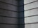 A corner of a building with a modern, minimalist design features horizontal concrete slabs. The surface has a textured appearance, showing light and shadow creating a stark contrast with a diagonal division between light and dark.
