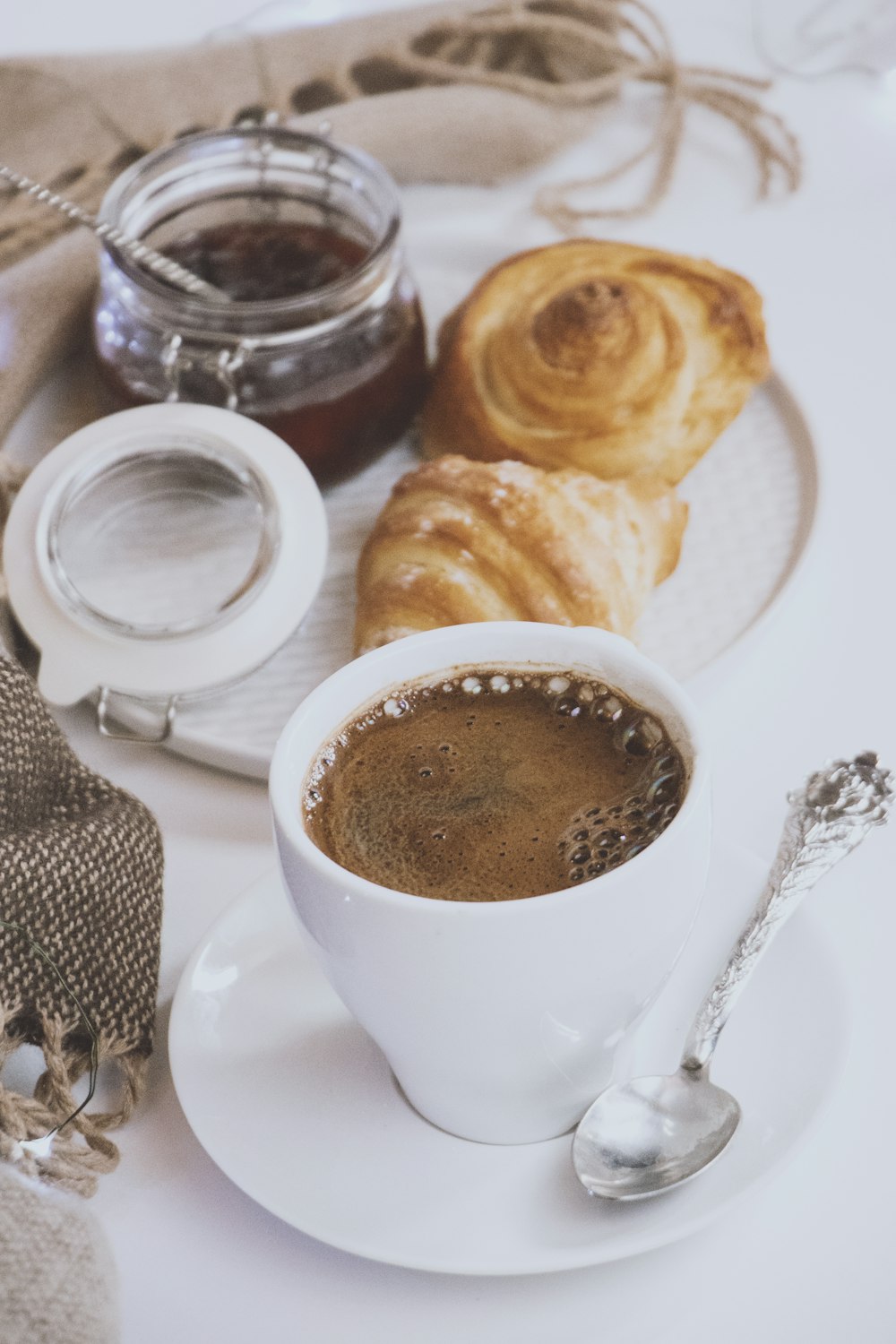 white ceramic mug filled with brown liquid on saucer near bread