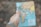 A hand holding a small world map focused on Europe, Africa, and parts of Asia. The background is blurred and earthy, suggesting an outdoor setting.