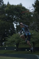 An action shot of a person mid-jump during an outdoor sports activity surrounded by lush greenery.