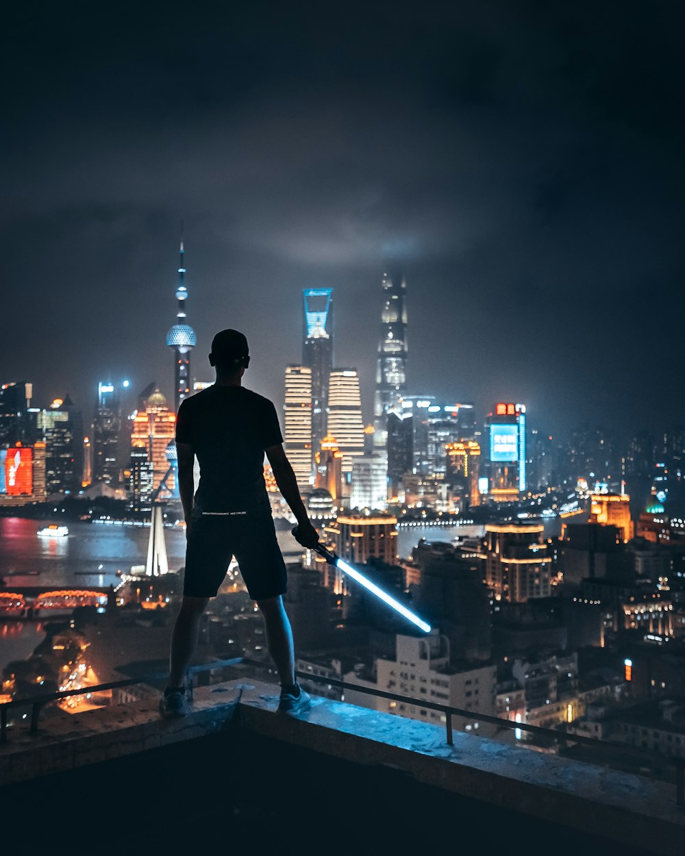 man holding lightsaber while standing on ledge overlooking city