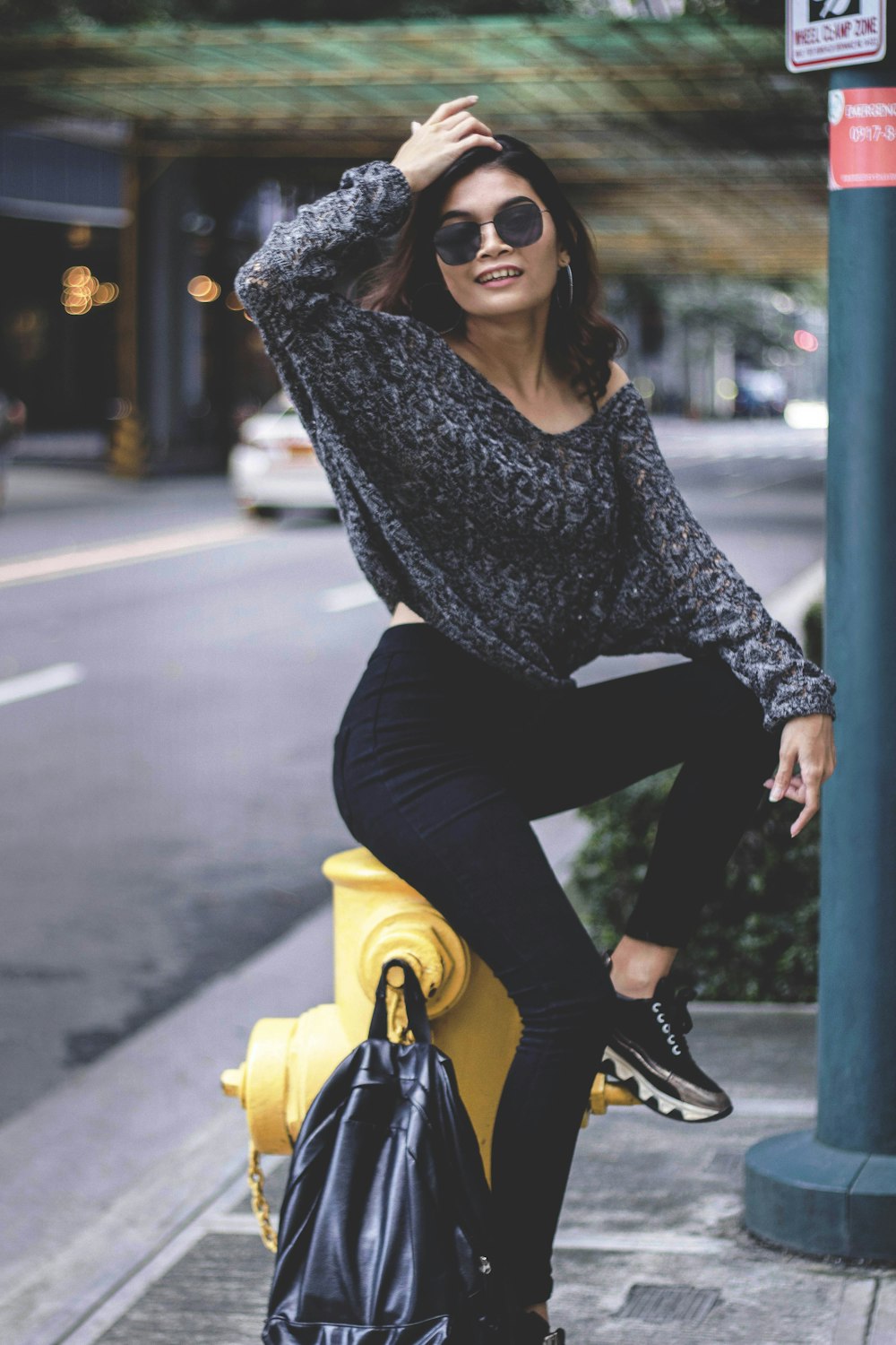 smiling woman wearing gray sweater and sunglasses sitting on yellow fire hydrant