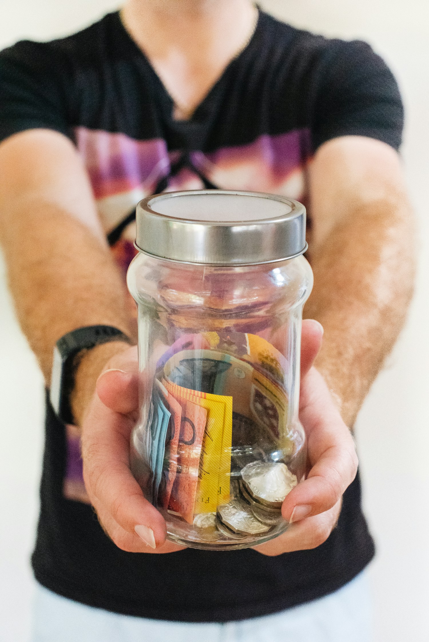 Person holding a jar containing cash and coins.