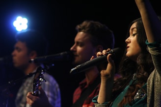 A trio of young men performing jazz music on stage with a microphone and instruments.