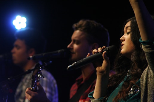 A trio of young men performing jazz music on stage with a microphone and instruments.