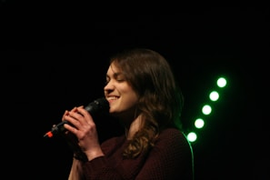 A female vocalist singing into a microphone with a joyful expression during a live show.