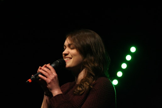 A person singing joyfully into a microphone with colorful lights in the background, capturing the essence of a lively karaoke session.
