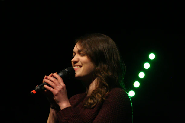 A cheerful woman singing karaoke with a microphone in a small, intimate bar setting.