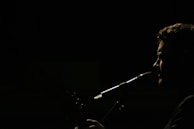 A silhouette of a person is captured in profile against a dark background, with light emphasizing their facial features and a microphone positioned near their mouth, suggesting they are singing or speaking.