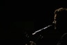 A silhouette of a person is captured in profile against a dark background, with light emphasizing their facial features and a microphone positioned near their mouth, suggesting they are singing or speaking.