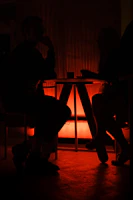 Softly lit scene of two people sharing a subtle, intimate glance across a table with scattered cards.