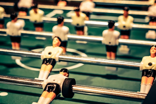 Several foosball player figures attached to rods are positioned on a green foosball table. The figures are wearing white shirts and black shorts, with the focus on one figure in the foreground.