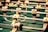 Several foosball player figures attached to rods are positioned on a green foosball table. The figures are wearing white shirts and black shorts, with the focus on one figure in the foreground.