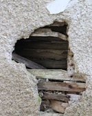 A section of a wall with a large hole exposes the wooden structural beams behind the plaster. The outer texture appears rough and worn, indicating age or damage.