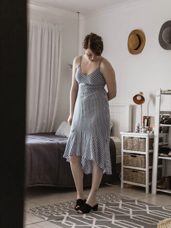 woman wearing black and white striped spaghetti strap dress standing beside bed frame