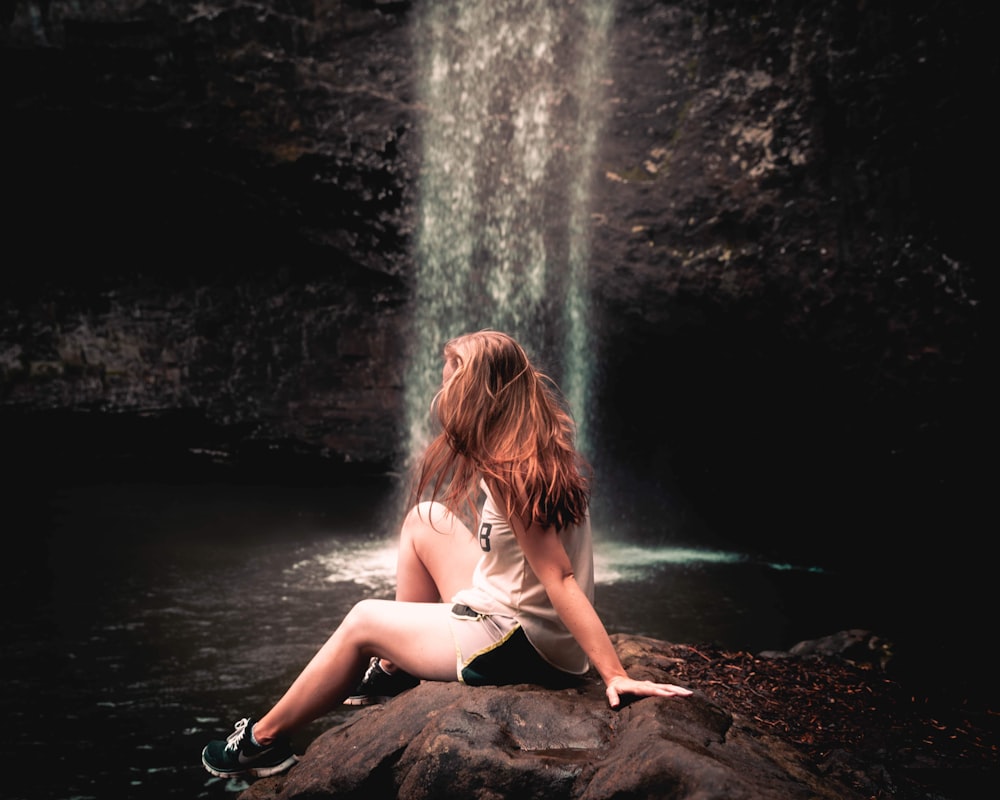 woman sitting on rock near waterfalls