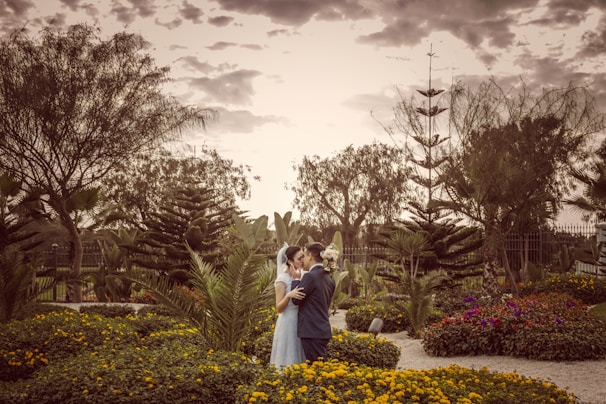 An intimate couple sharing a quiet moment in the manicured gardens under soft, muted navy skies