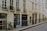 A quiet street with beige-colored residential buildings featuring multiple windows adorned with decorative wrought iron railings and potted plants. A small sign for 'Jean de Beauvais' is visible, adding a touch of character. The buildings exhibit classic urban architecture with subtle weathering.